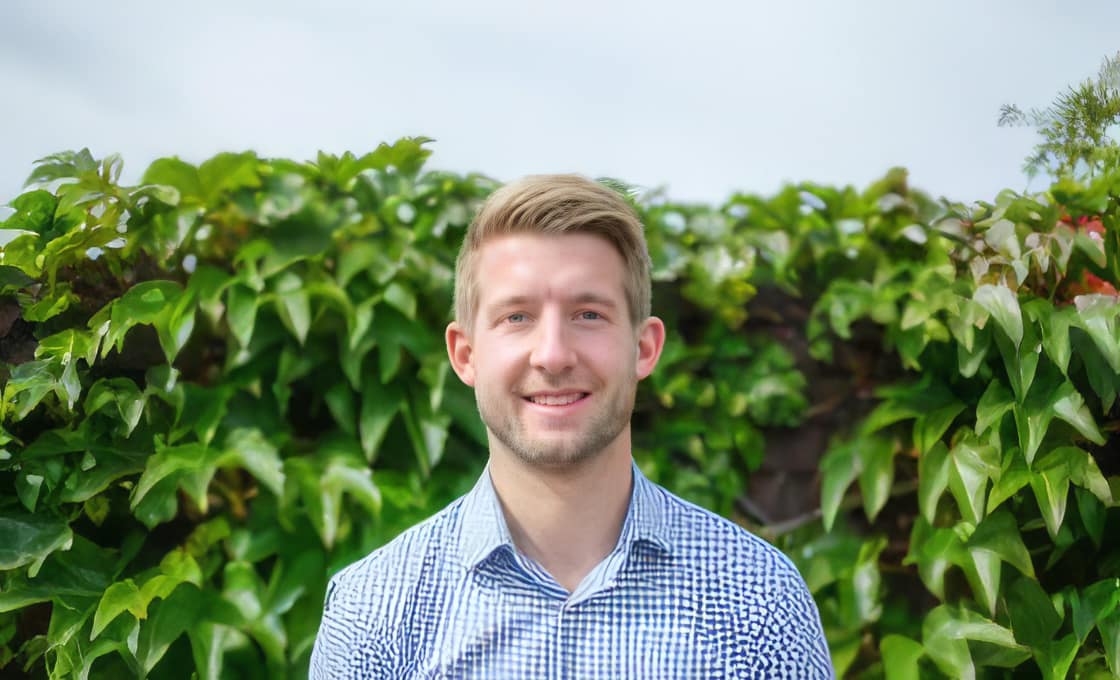 Smiling man standing in front of green leaves