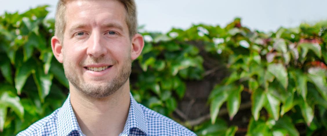 Smiling man standing outdoors near green leaves