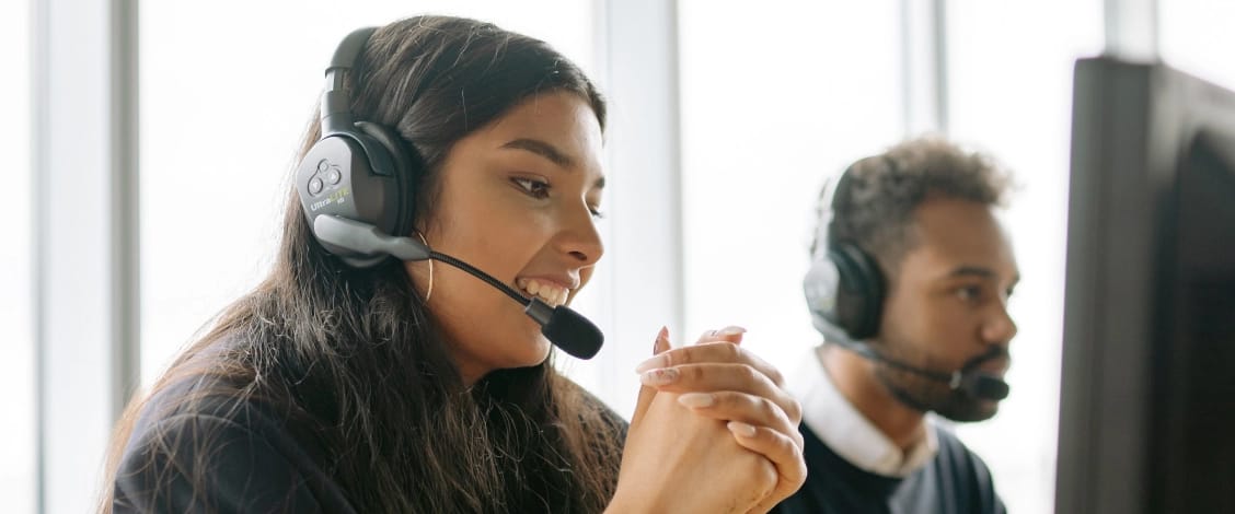 two customer service agents wearing headsets at computer desks.