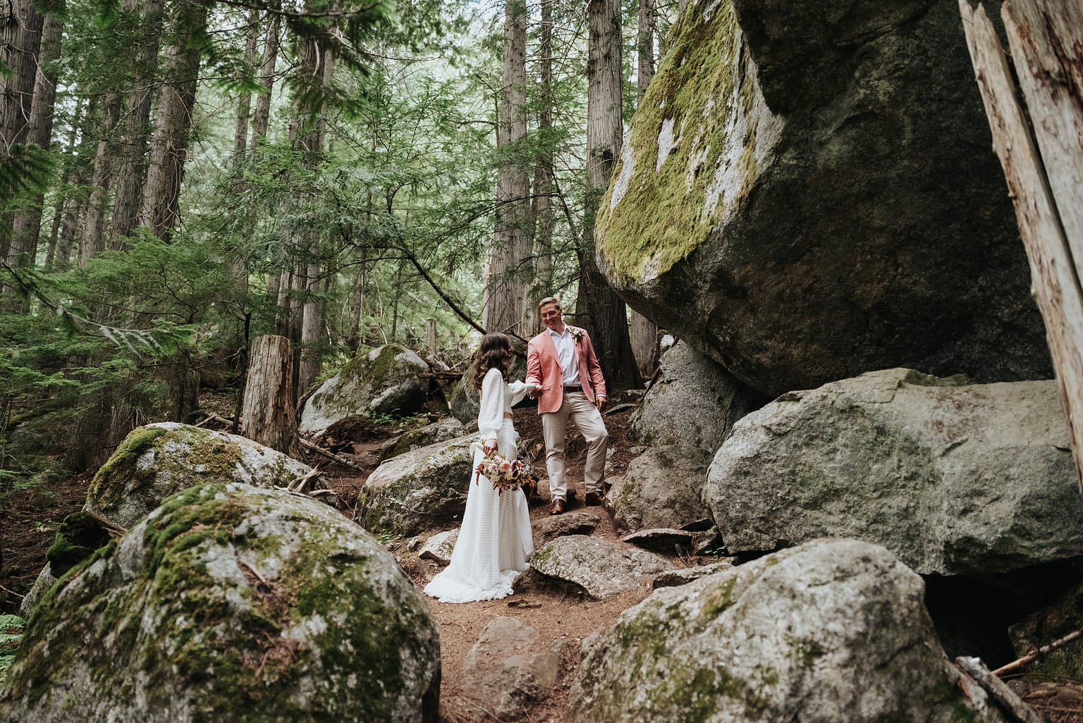 Couple walking in a forest with large rocks.