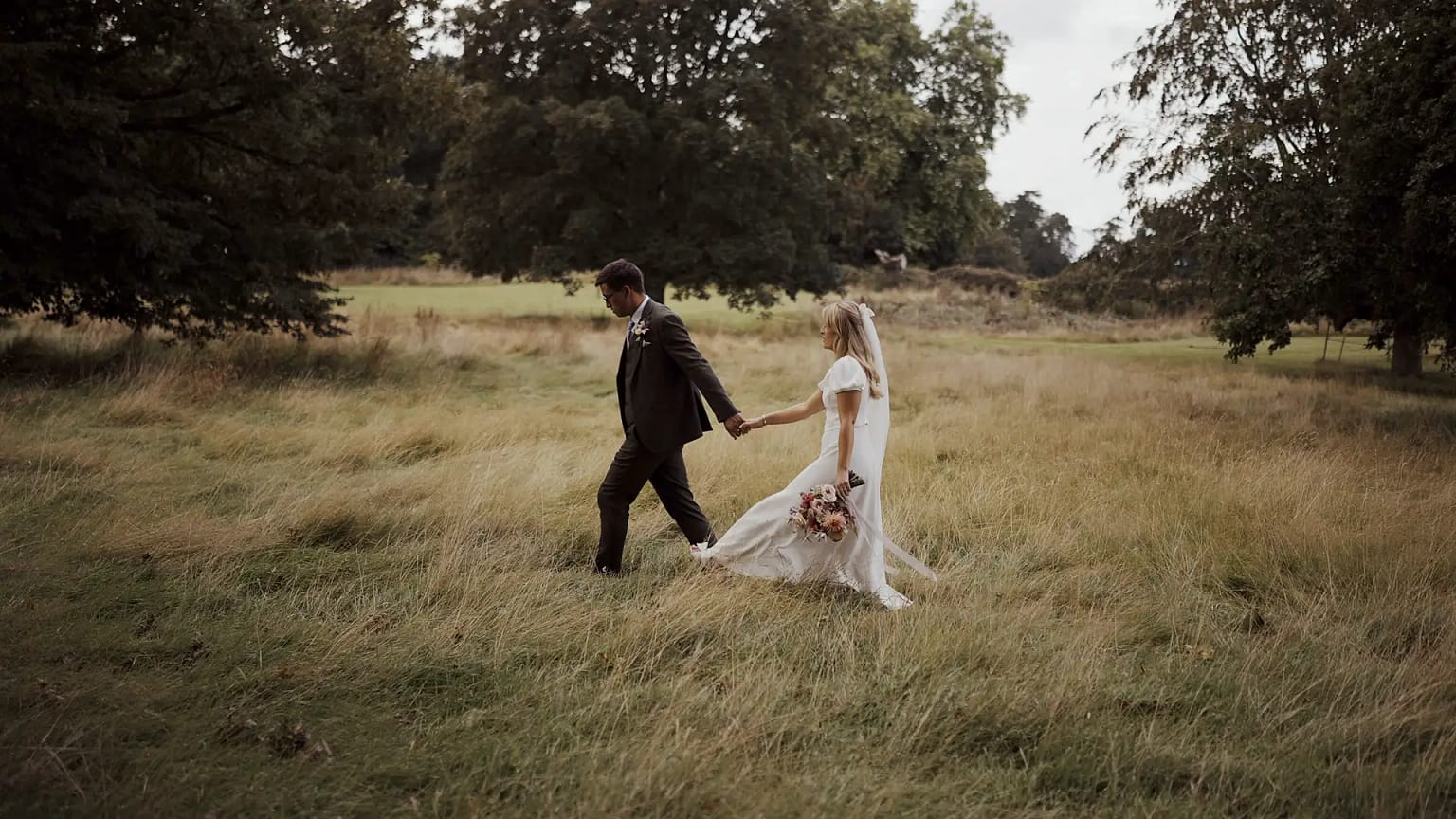 Couple walking hand-in-hand through grassy field