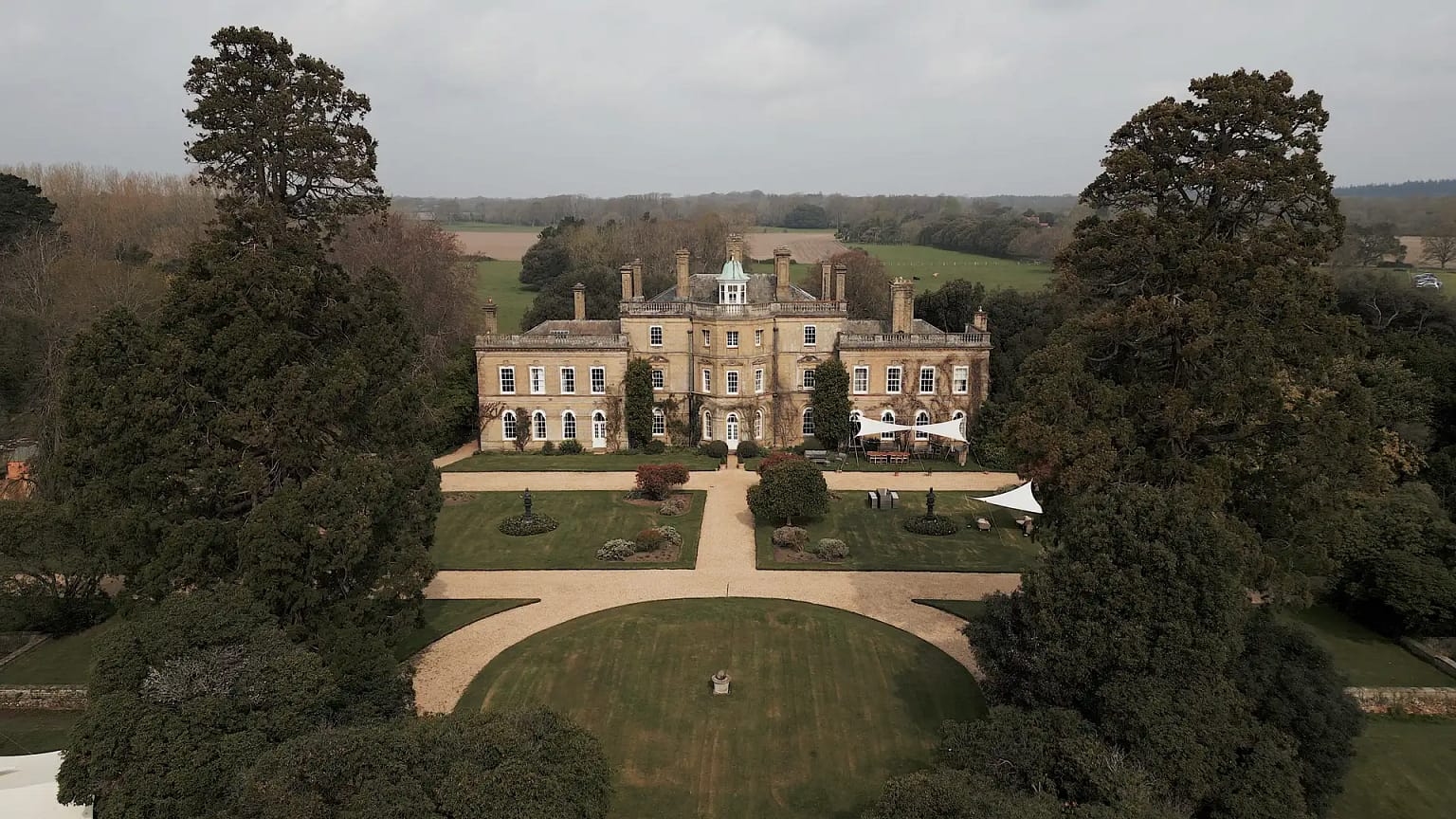 Historical mansion surrounded by gardens and trees.