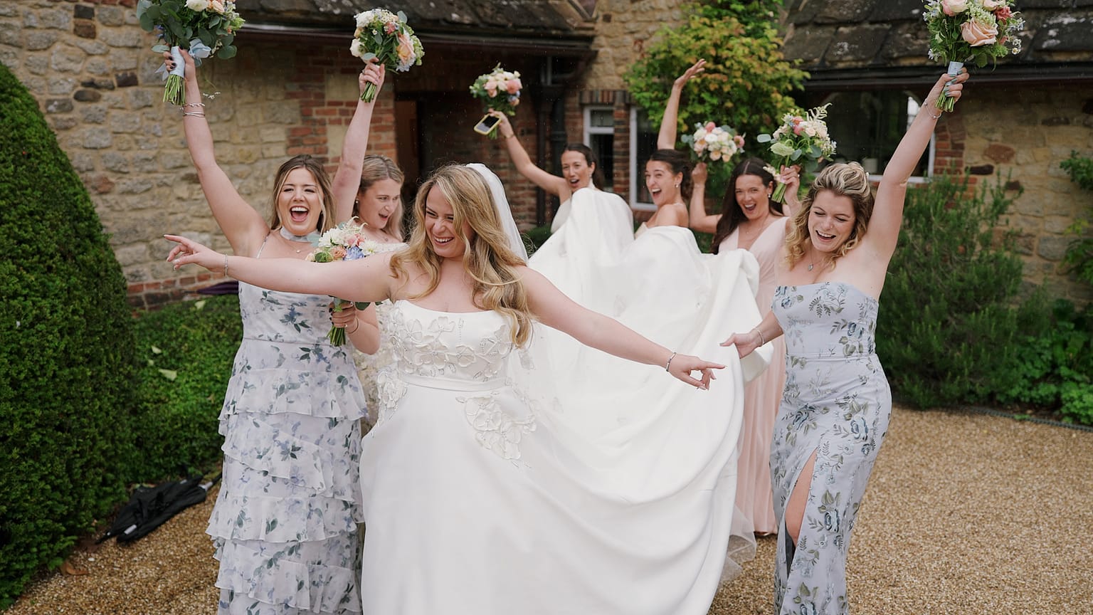 Bride and bridesmaids joyfully celebrating outside wedding venue.