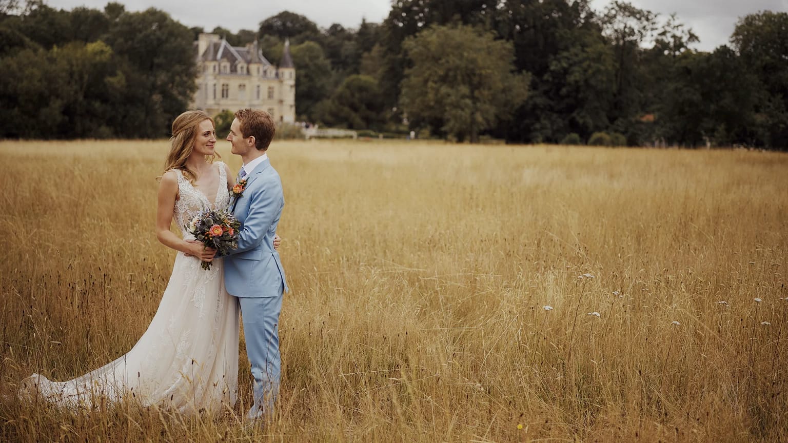 Bride and groom in field with castle backdrop.