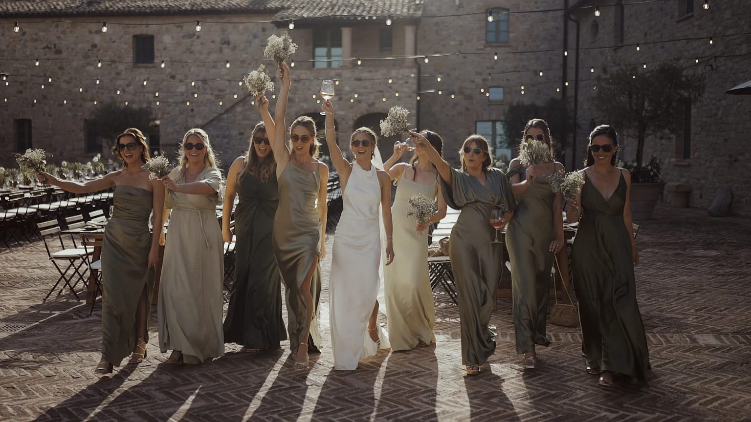 Bridesmaids celebrating outdoor wedding, holding flowers and drinks.
