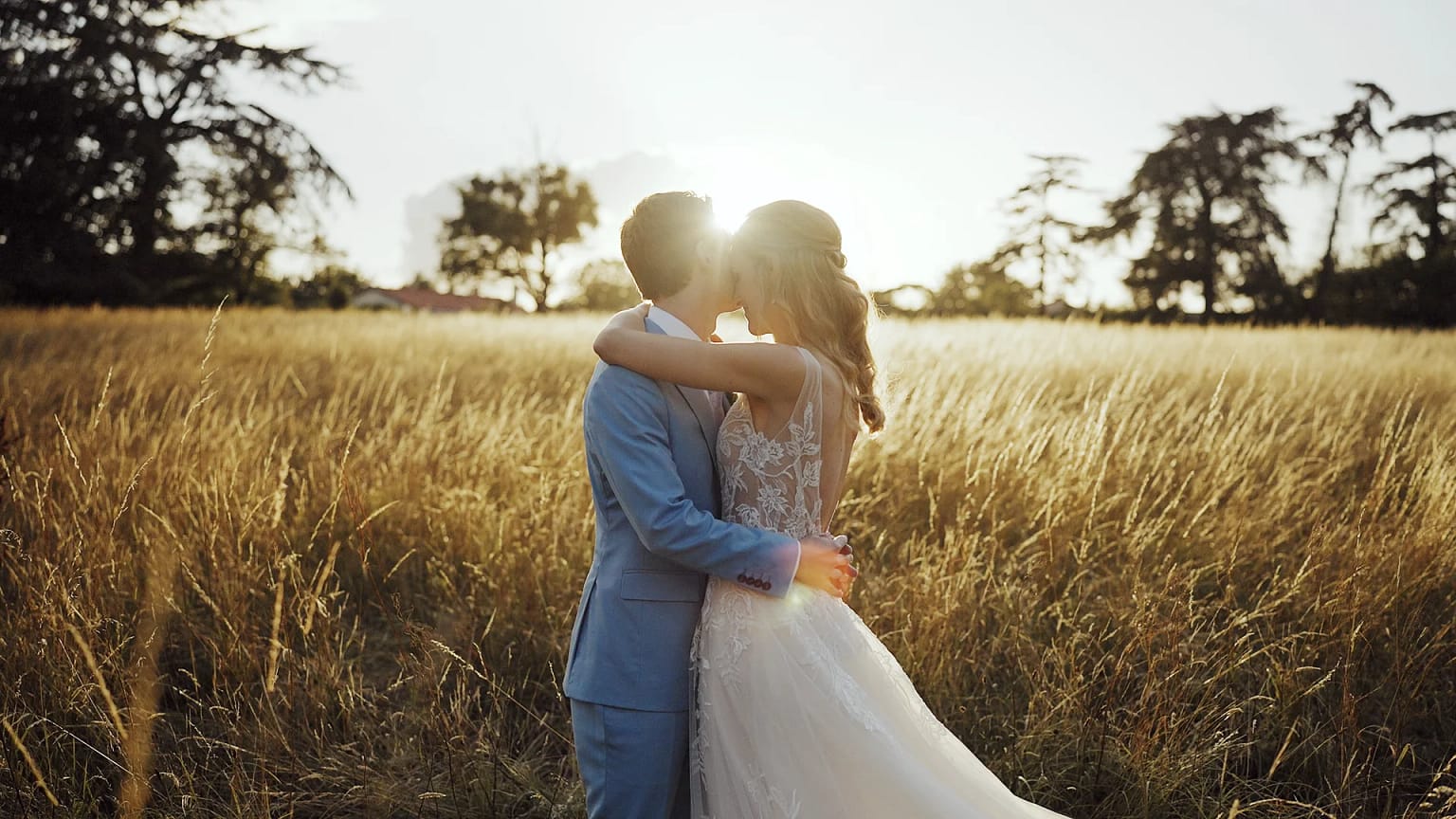 Couple kissing in sunlit field.