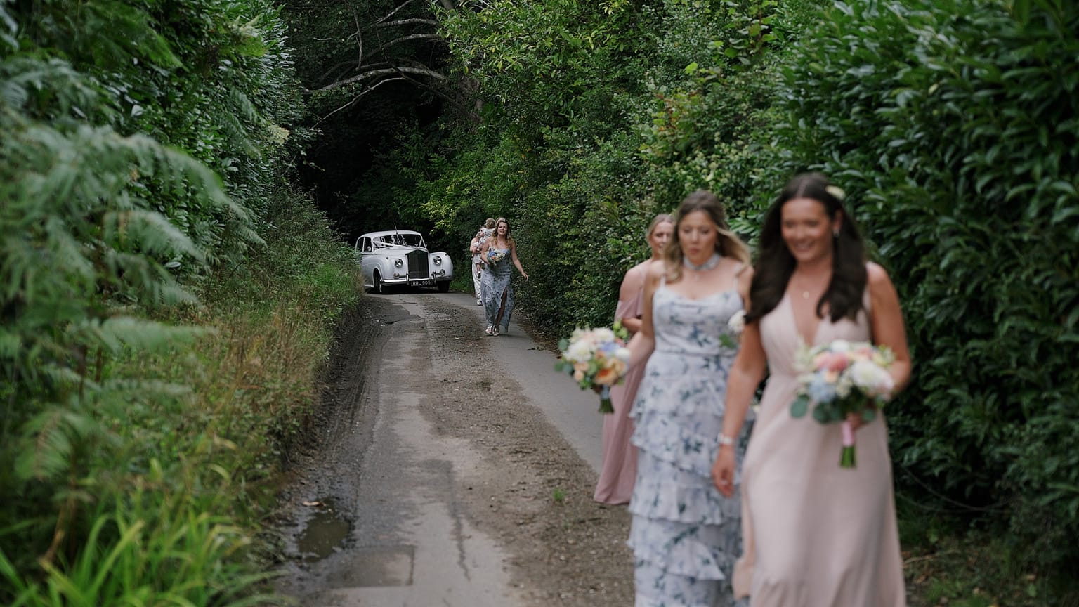 Bridesmaids walking down a country lane with flowers.