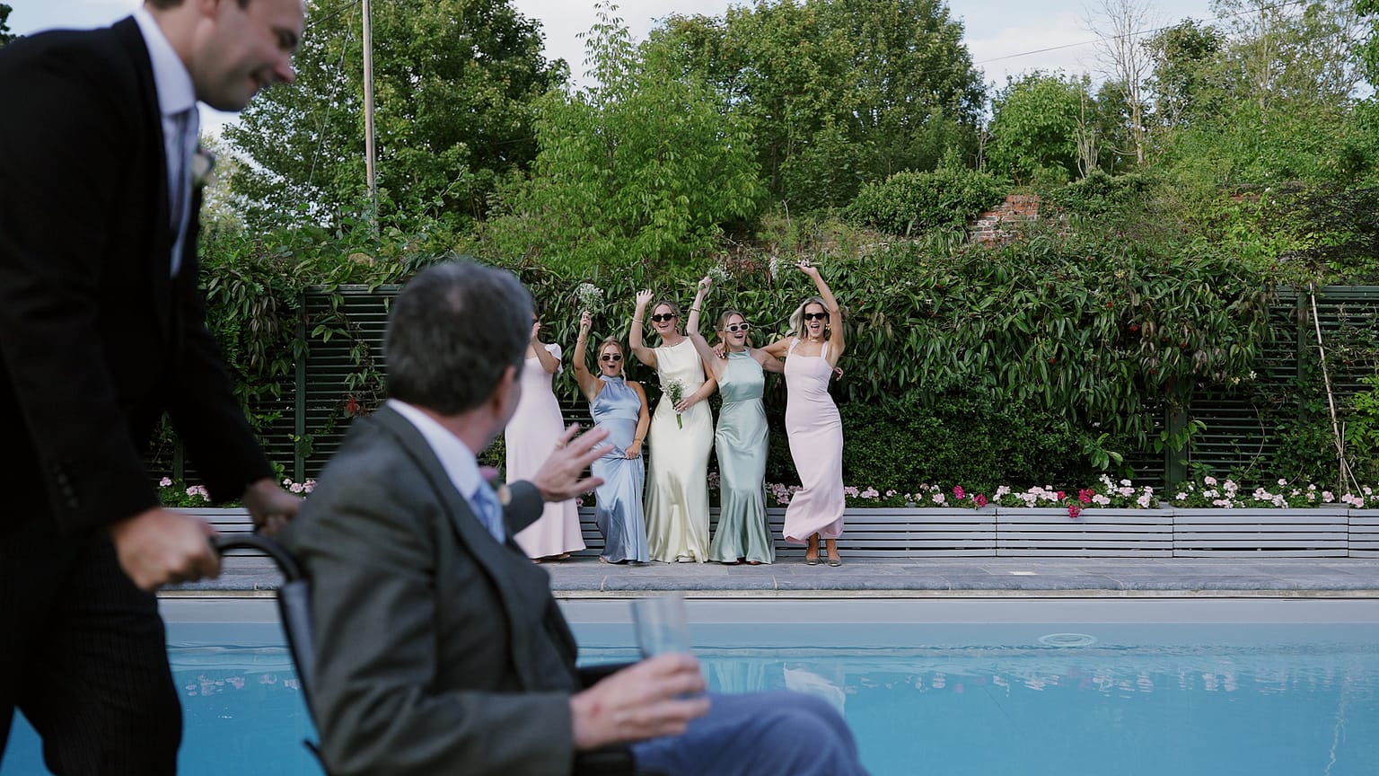 Bridesmaids cheering by pool as men approach