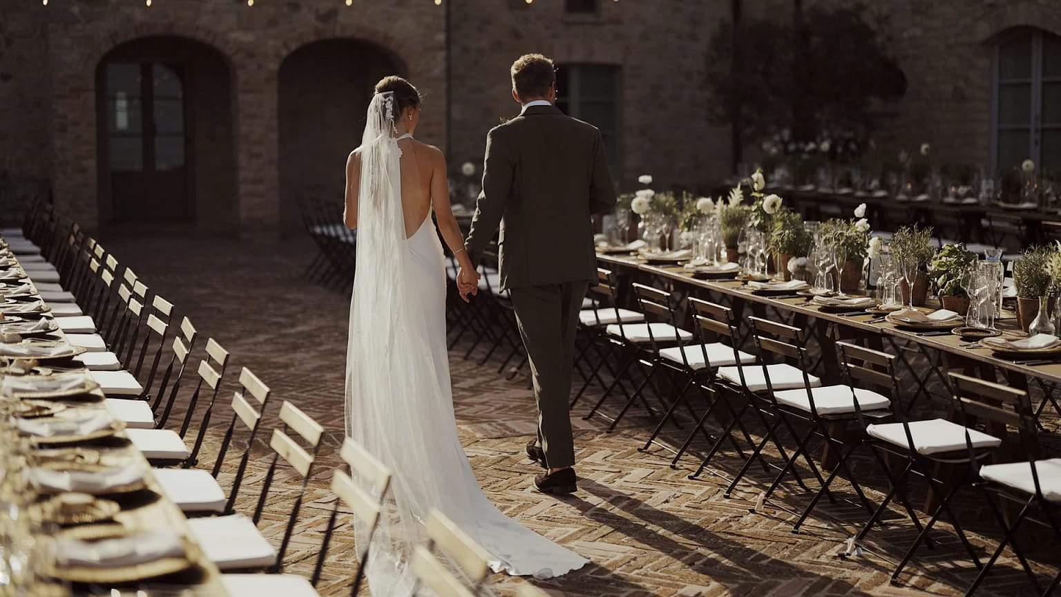 Bride and groom walking between decorated tables outdoors.