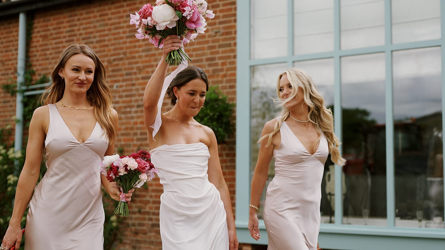 Three bridesmaids walking with flower bouquets.