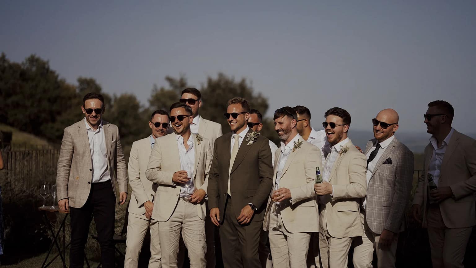 Groomsmen group in light suits and sunglasses outdoors.