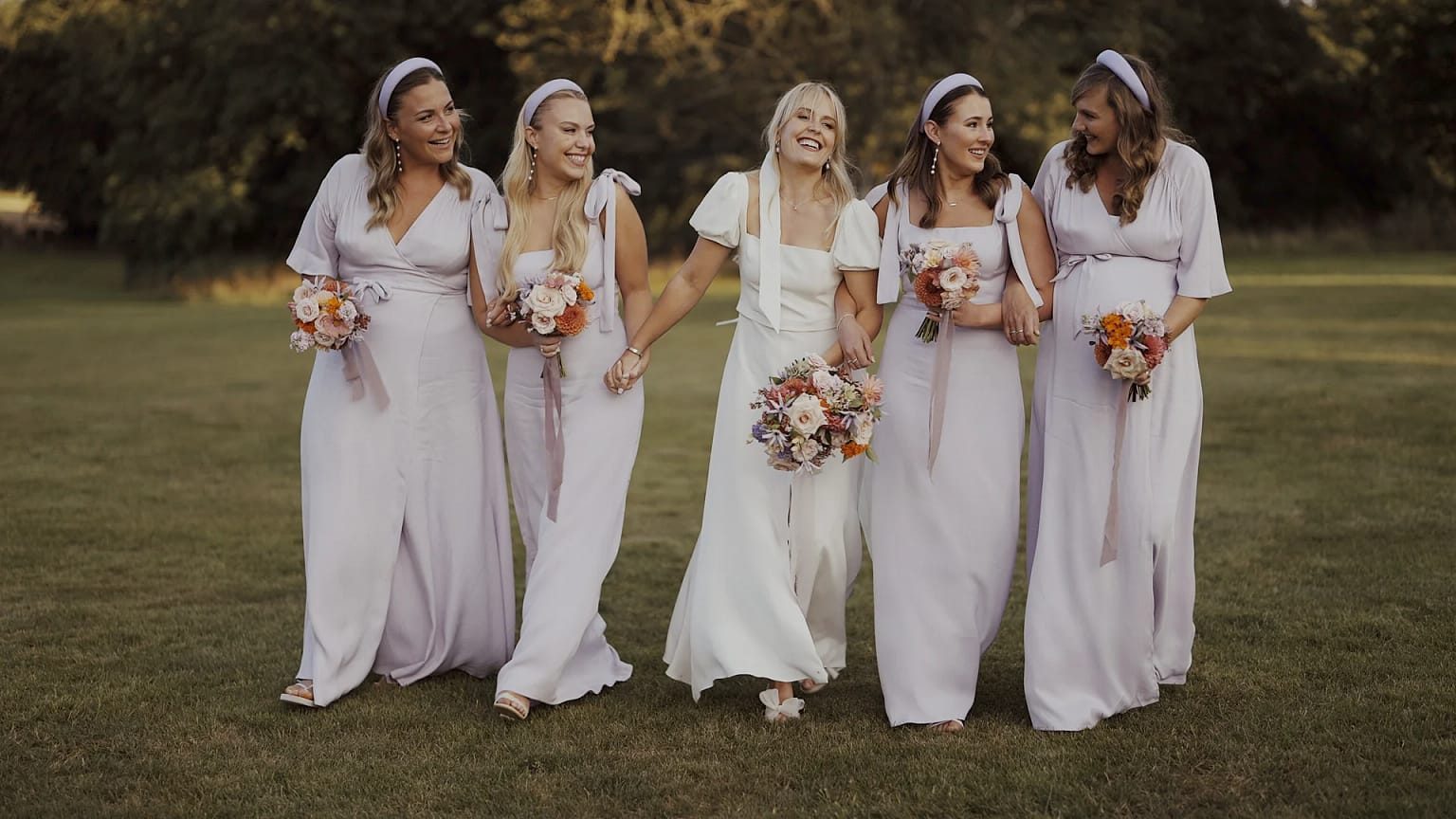Bridesmaids laughing with bride outdoors in lavender dresses
