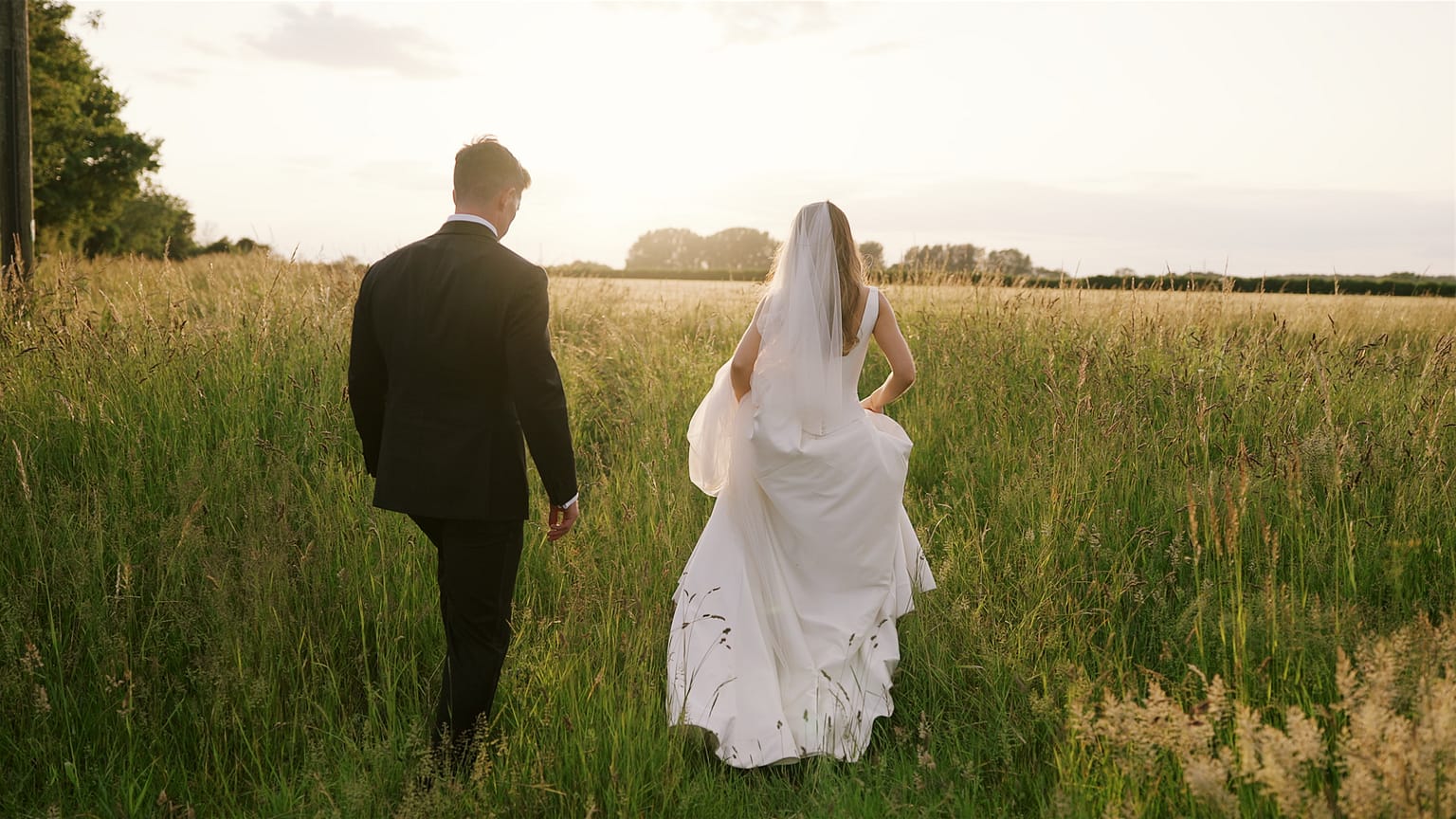 Bride and groom walking in a meadow at sunset.