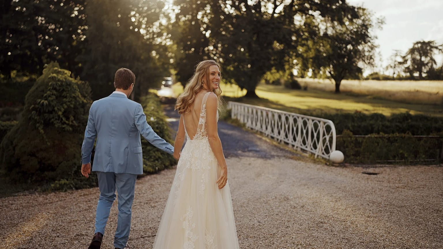 Bride and groom walking in sunlit garden.