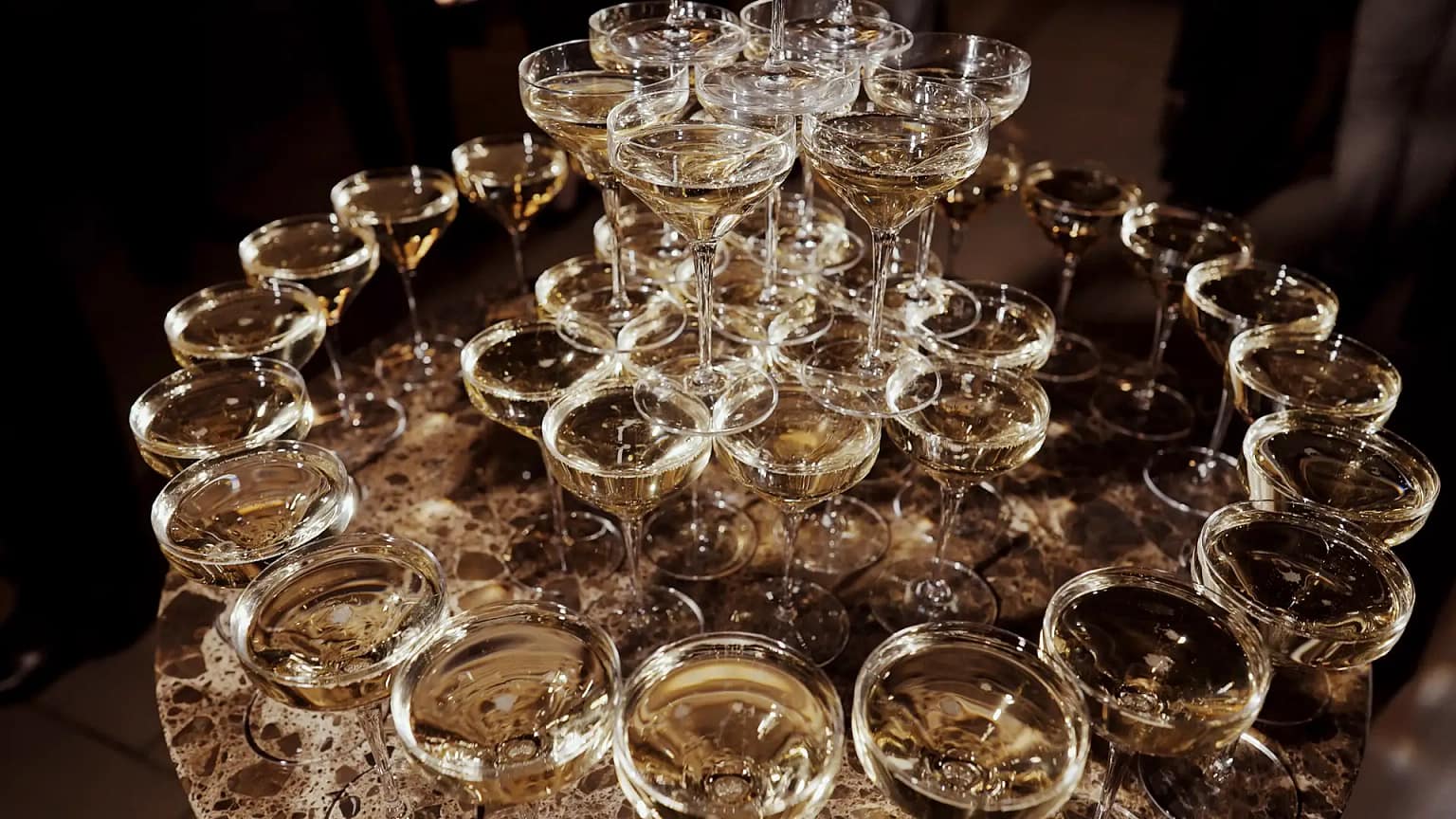 Champagne pyramid with filled glasses on marble table.