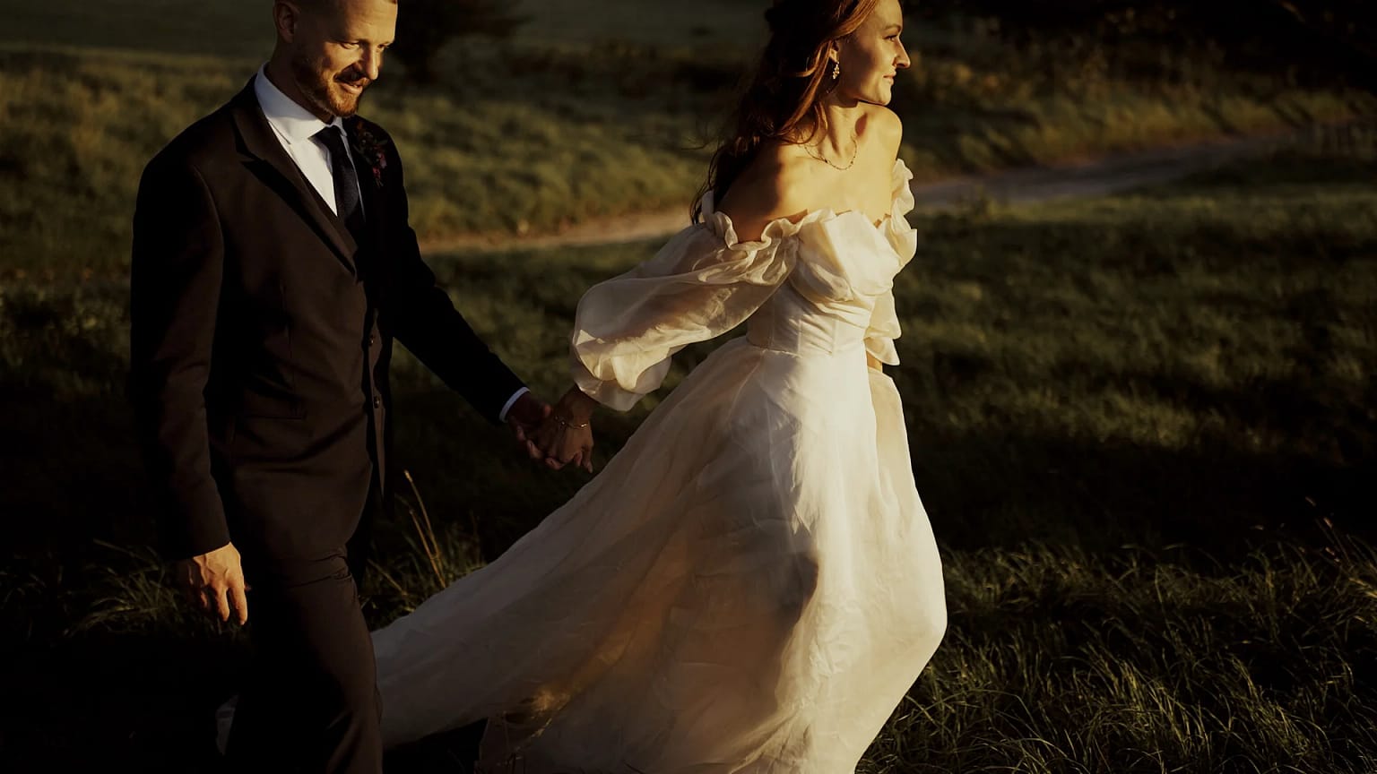 Bride and groom walking through sunlit field