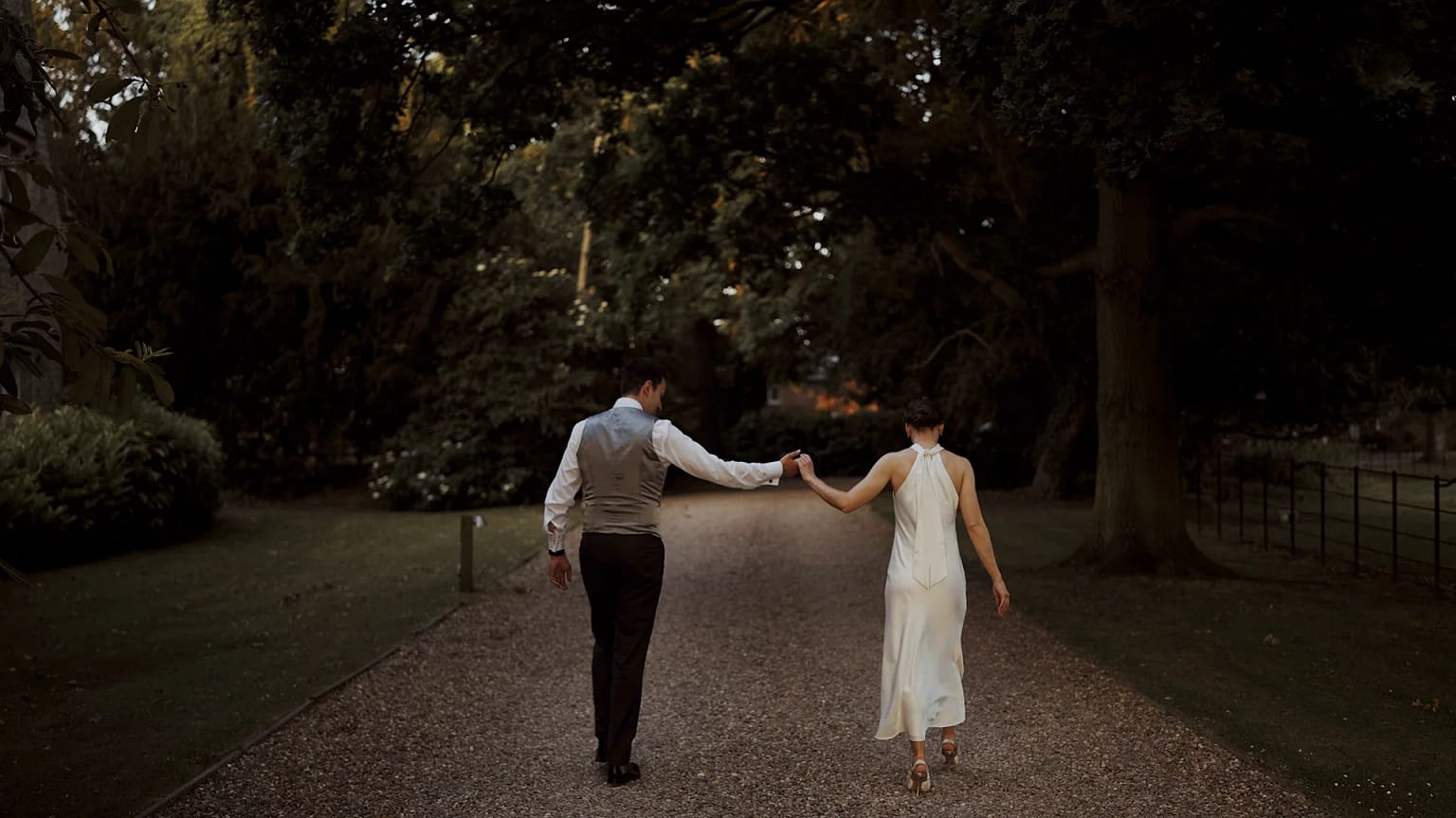 Couple walking hand-in-hand down forest path.