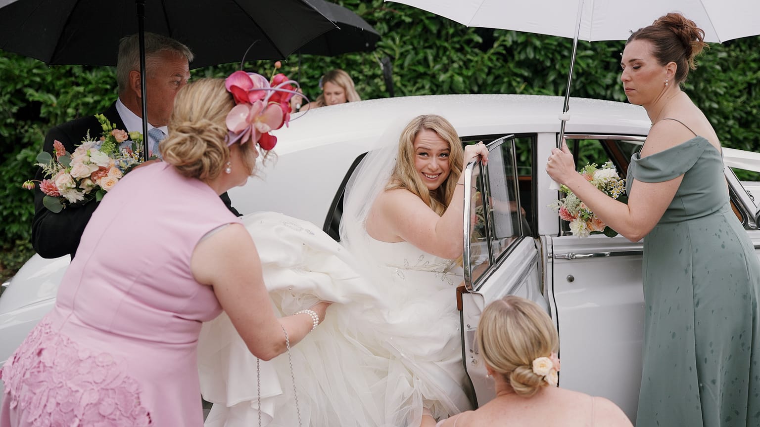 Bride exiting car with umbrella assistance