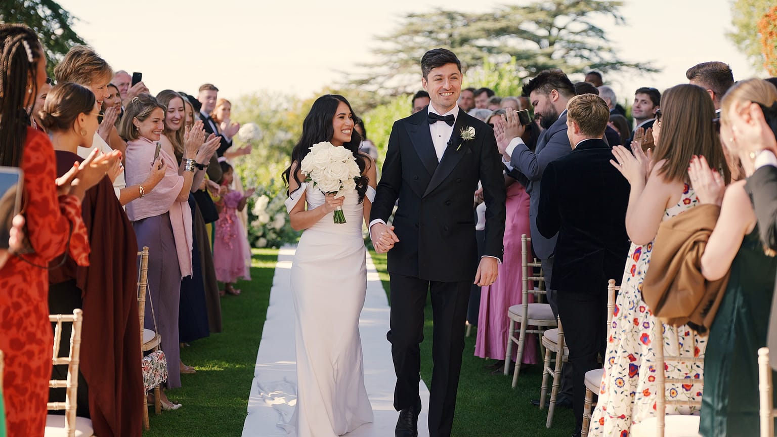 Bride and groom walk down aisle, guests clap.