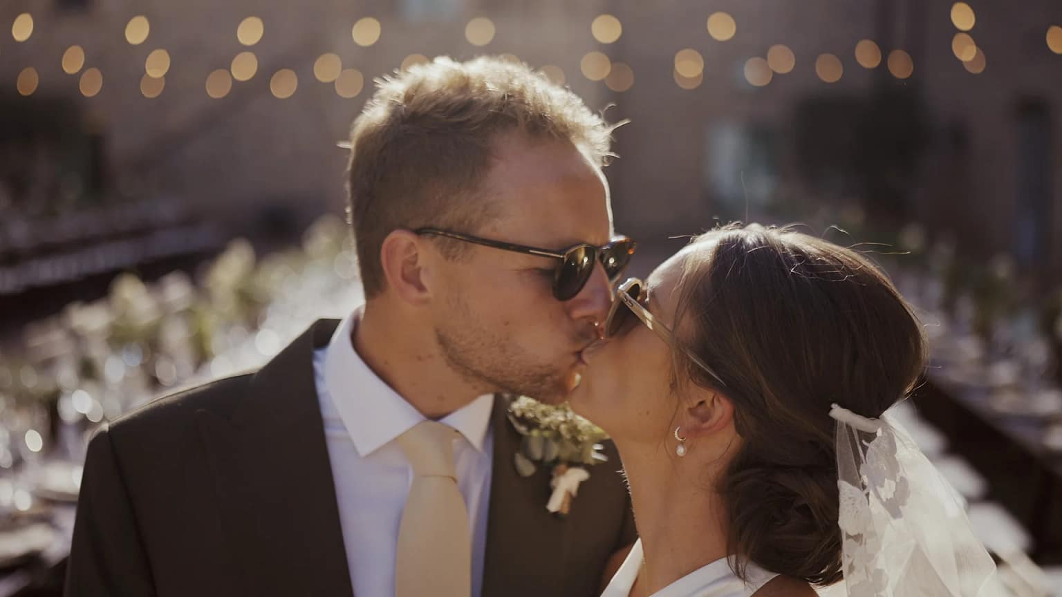 Newlyweds kissing under string lights at wedding.