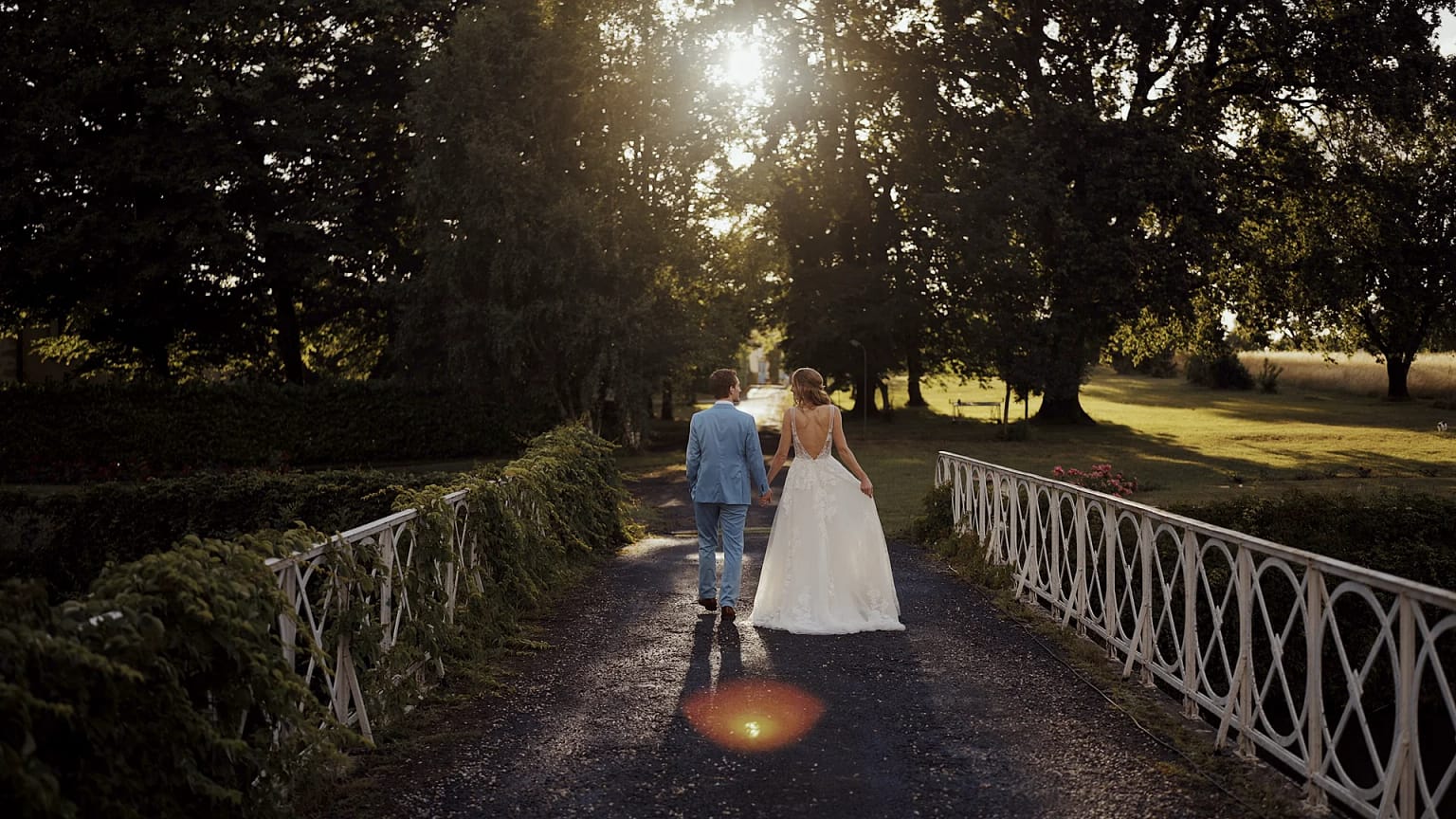 Bride and groom walking on bridge at sunset.