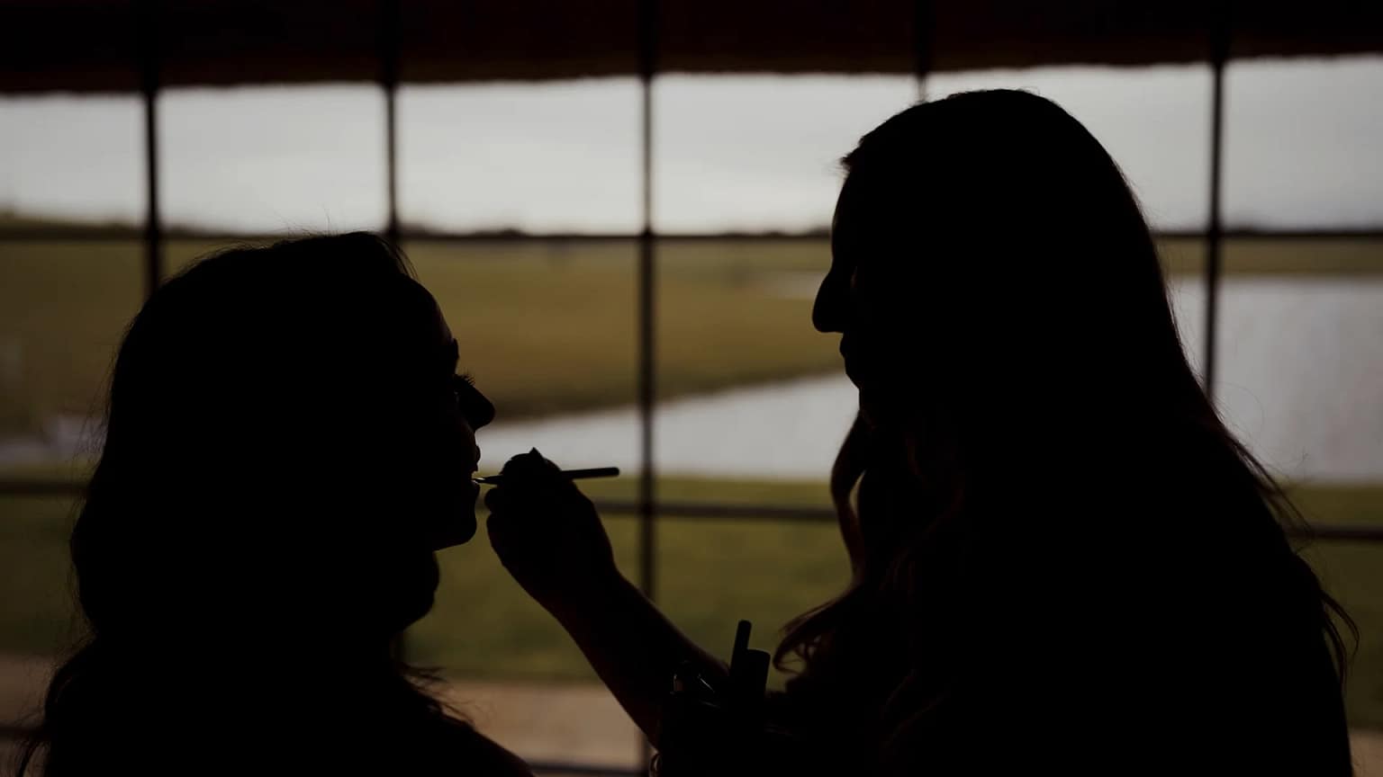 Silhouette of woman applying makeup near window.
