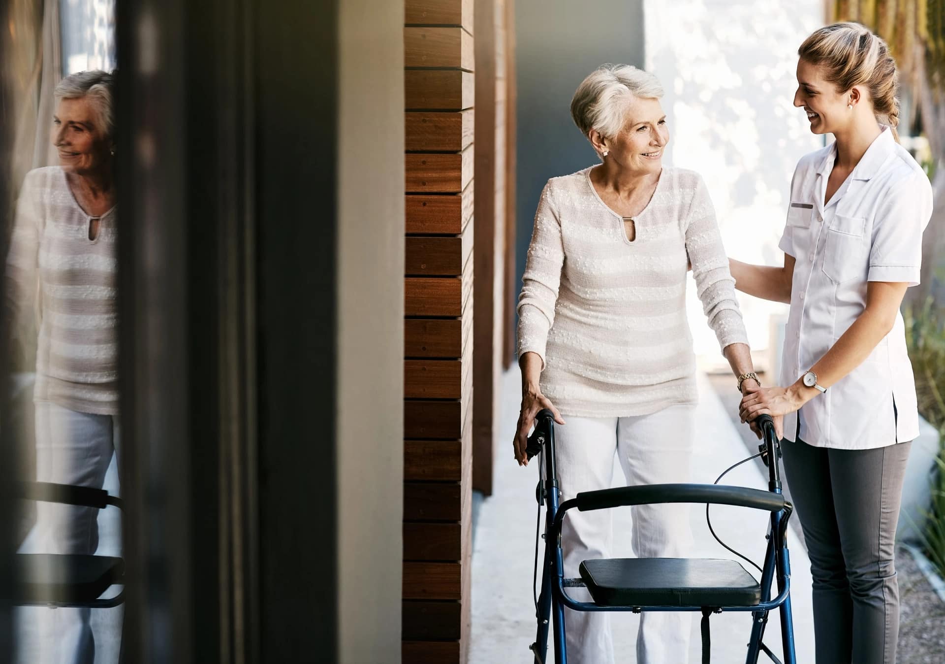 Caregiver assisting elderly woman with walker outside
