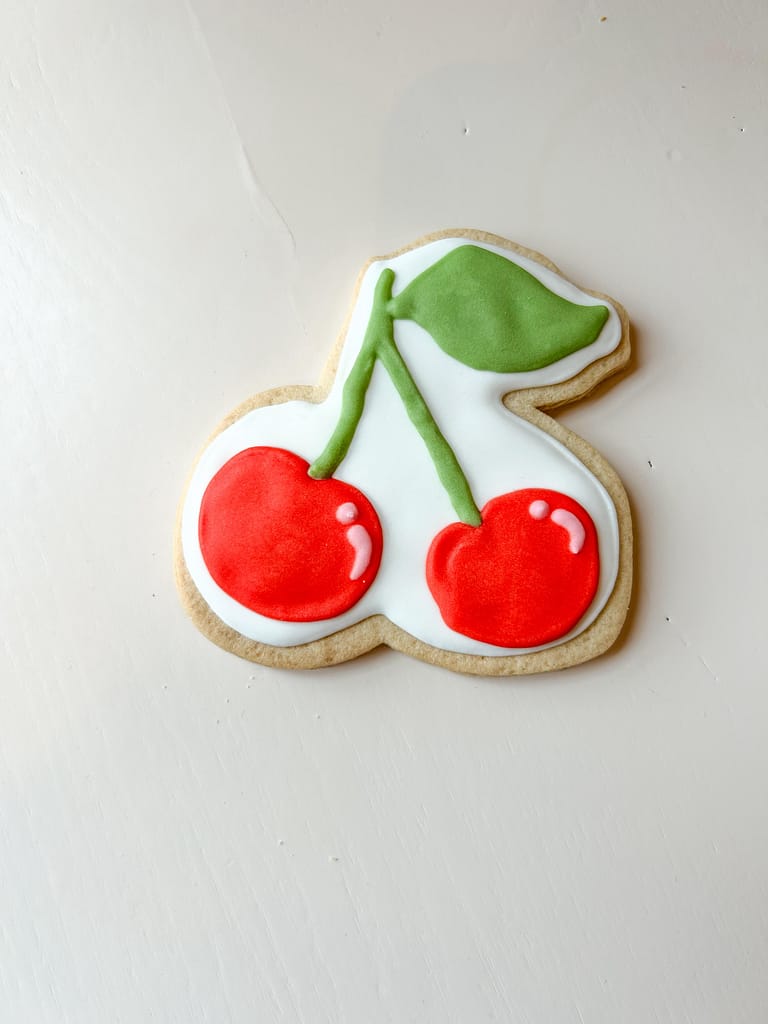 Cherry-shaped icing cookie on table.