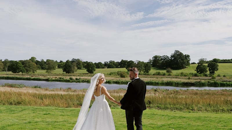 Bride and groom holding hands by picturesque lake.