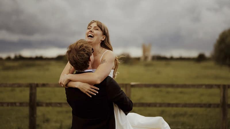 Bride laughing while groom lifts her outdoors.