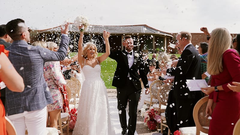 Bride and groom celebrate walking down confetti path.