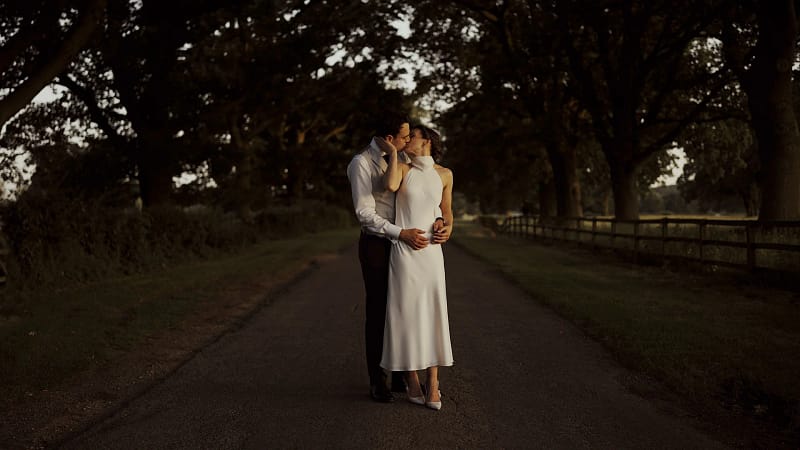Couple kissing on a tree-lined pathway.
