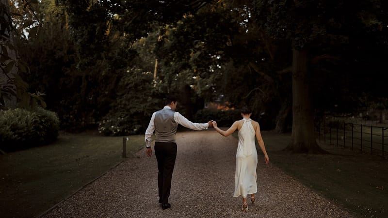 Couple walking hand-in-hand down forest path.