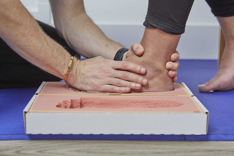 podiatrist placing patient's foot into foam impression box to take negative cast