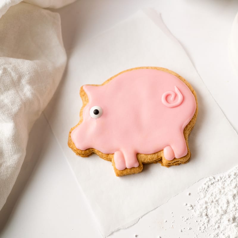 Pink pig-shaped iced biscuit on white background.