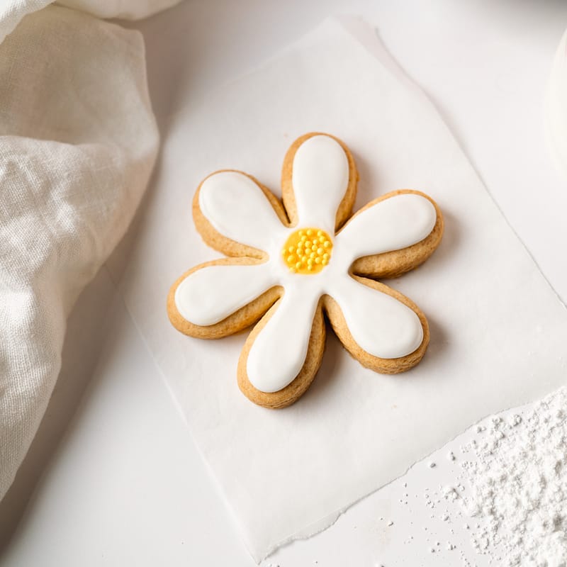 Flower-shaped iced biscuit on parchment paper.