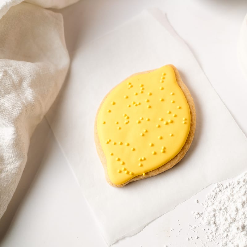 Lemon-shaped biscuit with yellow icing on paper.