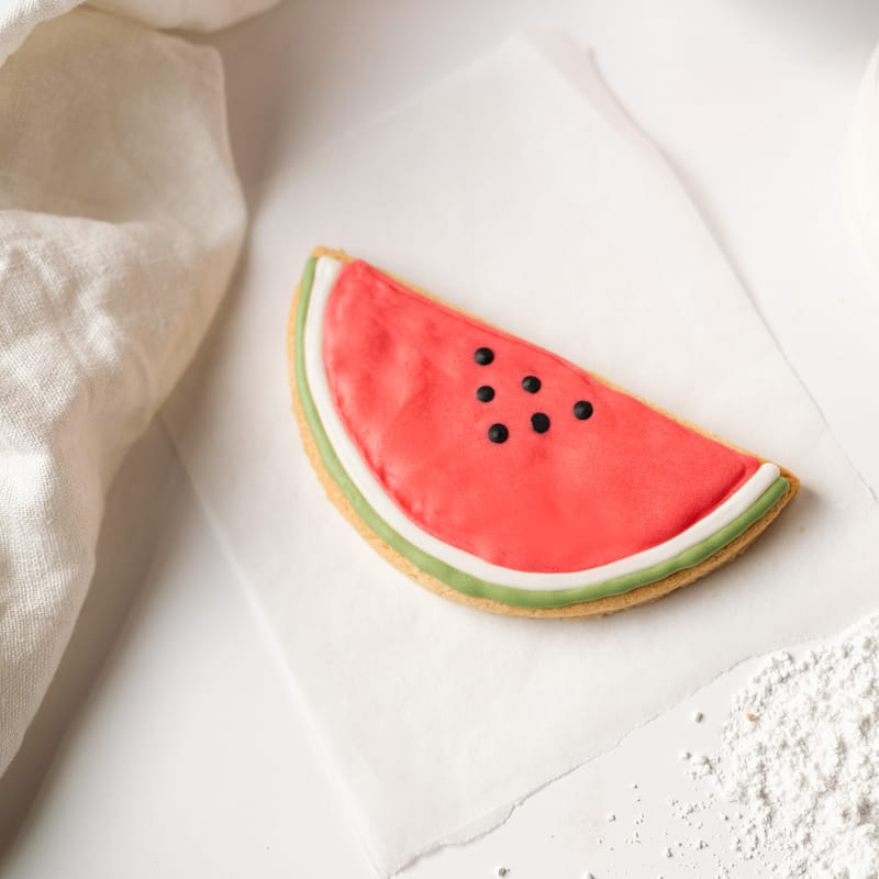 Watermelon-shaped cookie with icing on parchment paper.
