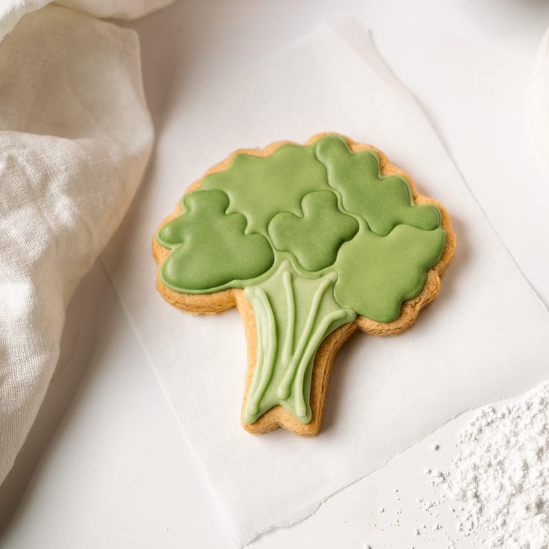 Broccoli-shaped iced biscuit on white paper.