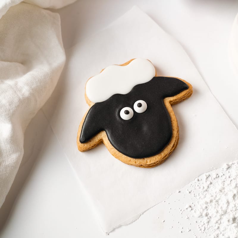 Sheep-shaped biscuit with black icing on parchment.