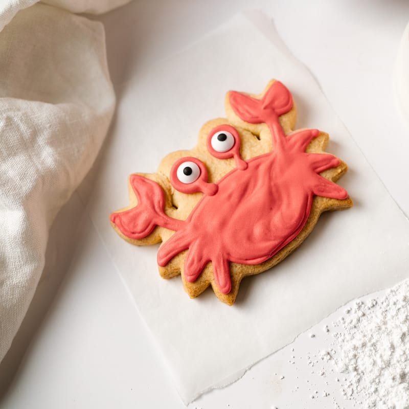 Red crab-shaped iced biscuit on parchment paper.