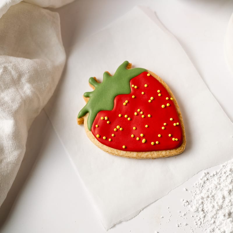Iced strawberry biscuit with sprinkles on parchment paper.