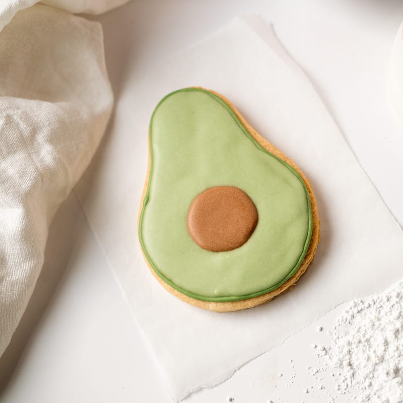 Avocado-shaped biscuit with green icing on paper.