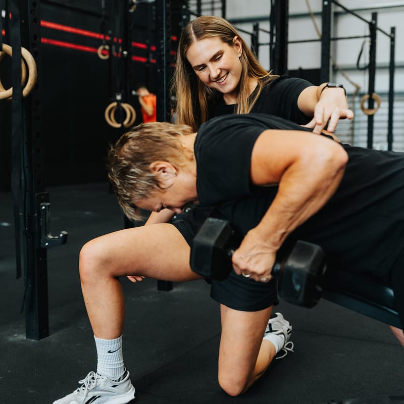 Personal trainer guiding client during dumbbell workout.